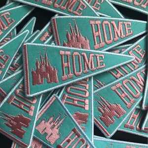 May include: A pile of teal blue felt pennants with pink embroidered text that reads "HOME" and a pink embroidered image of a castle.