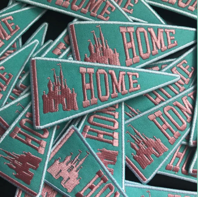May include: A pile of teal blue felt pennants with pink embroidered text that reads "HOME" and a pink embroidered image of a castle.