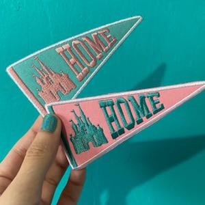 Peut inclure: Deux fanions en feutre de couleur rose et verte. Les deux fanions présentent un château stylisé et le mot "HOME" en broderie verte.