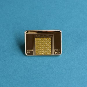 May include: Gold-colored metal pin with a depiction of a door with a geometric pattern. The text "This is the TVA" is printed on the pin.