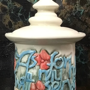 May include: White ceramic jar with a lid and a floral design. The jar has a blue inscription that reads "As for me and my house, we will serve the Lord."
