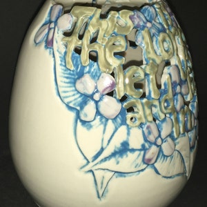 Peut inclure: Vase en céramique blanche avec un motif floral bleu et violet. Le vase a un motif découpé qui épelle "This is the love I send and I"