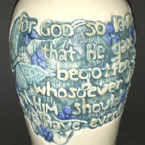 May include: White ceramic urn with a blue and green floral design and the text "For God so loved that He gave His only begotten Son, that whosoever believeth in Him should have everlasting life."