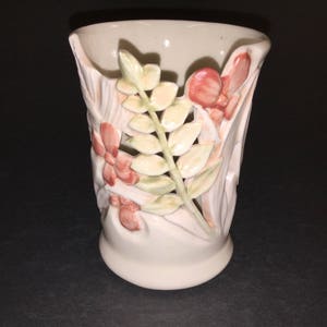 May include: A white ceramic vase with a floral design. The vase has a raised design of leaves and flowers in shades of pink and green.