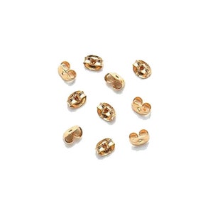 May include: Ten gold-colored earring backs. The backs are oval-shaped with a small hole in the center.