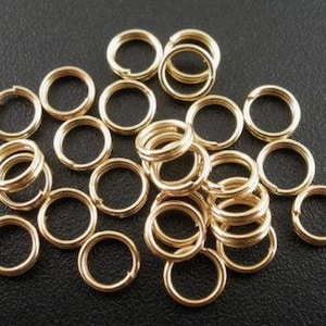 May include: A large pile of gold jump rings. The rings are small and round, and they are all the same size.