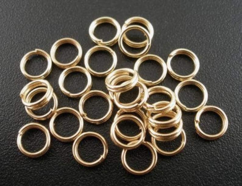 May include: A large pile of gold jump rings. The rings are small and round, and they are all the same size.