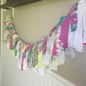 以下が含まれることがあります： 白、ピンク、緑、黄、青の布の切れ端を使ったカラフルな布のガーランド。ガーランドは、水玉模様、花柄、幾何学模様など、さまざまな模様の布で作られています。