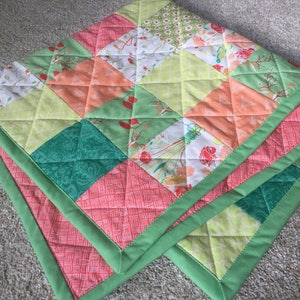 Puede incluir: Una colcha de retazos verde y naranja con un patrón de diamante. La colcha tiene un borde verde.