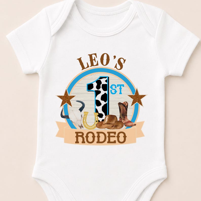 A white baby onesie with a graphic design featuring a cowboy hat, a horseshoe, and the text "LEO'S 1ST RODEO" printed on it.