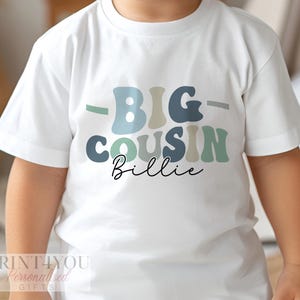 A child wearing a white t-shirt with the text "BIG COUSIN BILLIE" printed on it.