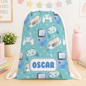 Può includere: Un sacco con coulisse turchese con un motivo di controller di videogiochi blu, console portatili e spade. Il nome "OSCAR" è visualizzato in un ovale bianco e blu. La borsa ha coulisse bianche.