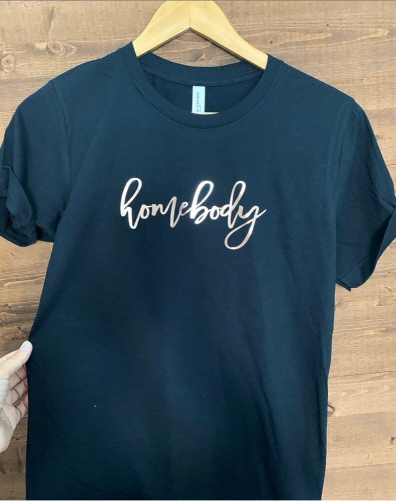 May include: A black t-shirt with the word "homebody" written in rose gold script.