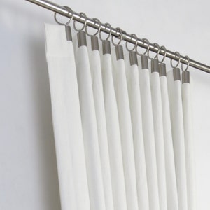 May include: White curtains with silver rings hanging on a silver curtain rod.