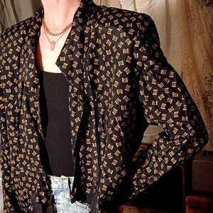 May include: A black and gold patterned blouse with a long sleeve and a tie at the neck.