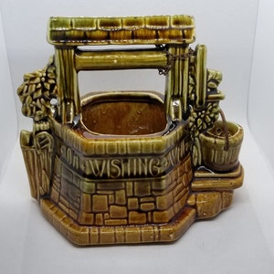 May include: A brown and green ceramic wishing well planter with a brick design and the words "For Wishing Well" on the front. The well has a small bucket and a chain hanging from the top.