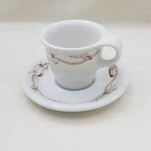 May include: A white ceramic teacup and saucer set with a brown nautical design. The design features a rope, a barrel, a gun, and an anchor.