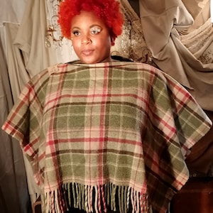 May include: A green, pink, and white plaid poncho with fringe trim. The poncho is made of a soft, woven fabric.