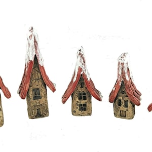 Könnte beinhalten: Fünf Miniaturhäuser aus Keramik mit roten und weißen Dächern. Die Häuser sind in einer Reihe vom größten zum kleinsten angeordnet.