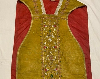 May include: A gold and red liturgical vestment with intricate embroidery. The vestment features a central design with floral motifs and a cross. The fabric is a rich, textured material.