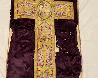 May include: A purple velvet chasuble with gold and silver embroidery. The embroidery features a lamb, floral designs, and other religious motifs.