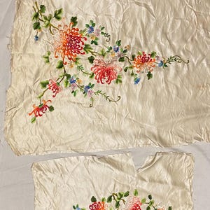 以下が含まれることがあります： 白い絹の生地2枚に刺繍された花の模様。花はピンク、赤、オレンジ、黄色で、緑の葉がついています。