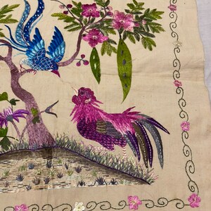 May include: Embroidered artwork depicting a blue bird perched on a branch with pink flowers, a pink rooster standing on a grassy mound, and a decorative border of green swirls and pink flowers.