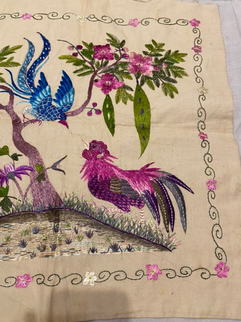 May include: Embroidered artwork depicting a blue bird perched on a branch with pink flowers, a pink rooster standing on a grassy mound, and a decorative border of green swirls and pink flowers.