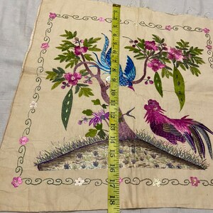 May include: A beige fabric panel with embroidered birds and flowers. The birds are a blue and white bird and a pink and purple bird. The flowers are pink and white. The panel is surrounded by a decorative border.