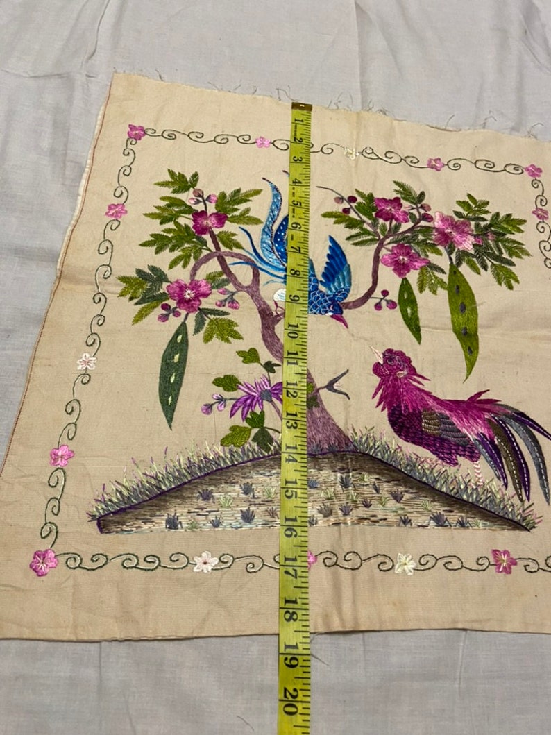 May include: A beige fabric panel with embroidered birds and flowers. The birds are a blue and white bird and a pink and purple bird. The flowers are pink and white. The panel is surrounded by a decorative border.