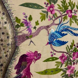 May include: Embroidered wall hanging featuring two birds with colourful plumage, perched on a branch with pink flowers and green leaves. The background is a beige fabric.