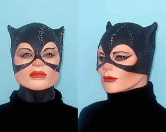 May include: A woman wearing a black catsuit with a black mask and ears. The mask has a black eye mask with a white outline. The woman has red lipstick and black eyeliner.