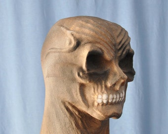 May include: A detailed, brown skull mask with hollow eye sockets and a prominent jawline. The mask has a textured surface and is designed to be worn. The teeth are white, and the overall appearance is weathered.