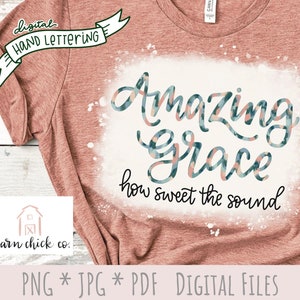 May include: A pink t-shirt with a white splatter design featuring the text "Amazing Grace how sweet the sound" in a blue and pink patterned font.
