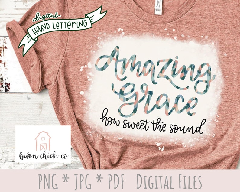 May include: A pink t-shirt with a white splatter design featuring the text "Amazing Grace how sweet the sound" in a blue and pink patterned font.