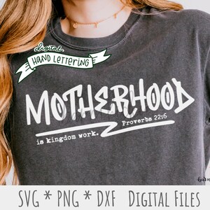 May include: A gray t-shirt with white text that reads "digital hand lettering MOTHERHOOD Proverbs 22:6 is kingdom work."