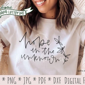 May include: White t-shirt with black hand-lettered text that reads "Hope in the unknown" with a floral design. The text is in a modern calligraphy style.
