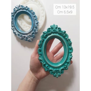 May include: Two oval-shaped picture frames with ornate details. The larger frame is 13 inches by 19.5 inches and the smaller frame is 6.5 inches by 9 inches. The larger frame is silver and the smaller frame is teal.