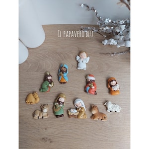 May include: A set of 10 small, colorful figurines depicting the Nativity scene. The figures include Mary, Joseph, baby Jesus, an angel, three wise men, a camel, a donkey, and a sheep. The figurines are made of ceramic and have a painted finish.