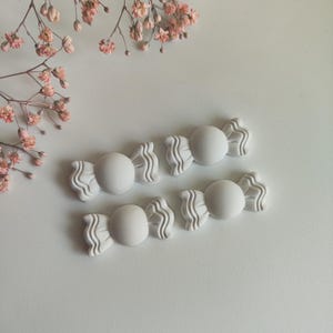 Può includere: Quattro stampi in silicone a forma di caramella di colore bianco. Gli stampi hanno la forma di un caramella con un centro arrotondato e due estremità curve.
