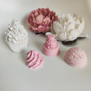 Può includere: Un set di cinque decorazioni per torte rosa e bianche, tra cui un cupcake, una torta nuziale, un vortice di glassa e due palline di gelato. Le decorazioni sono realizzate in un materiale liscio e bianco e sono perfette per aggiungere un tocco di dolcezza a qualsiasi progetto artigianale.