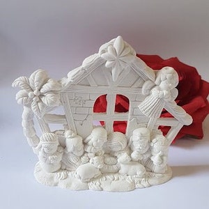 Puede incluir: Escena de la natividad de cerámica blanca con una pequeña casa, una palmera y figuras de María, José y el niño Jesús. Las figuras están de pie frente a la casa, y la palmera está a la izquierda de la casa.