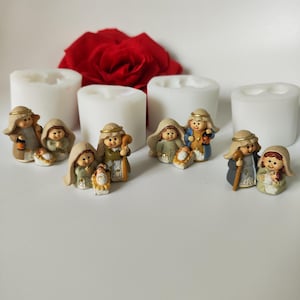 Könnte beinhalten: Ein Satz mit vier weißen Silikonformen zum Herstellen von Miniatur-Krippenfiguren. Die Formen sind in einer Reihe auf einer weißen Oberfläche angeordnet. Es gibt auch mehrere kleine, bemalte Figuren der Weihnachtsgeschichte, darunter Maria, Josef, das Jesuskind und ein Hirte.
