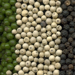 May include: A close-up of three types of peppercorns: green, white, and black. The peppercorns are arranged in three vertical rows.