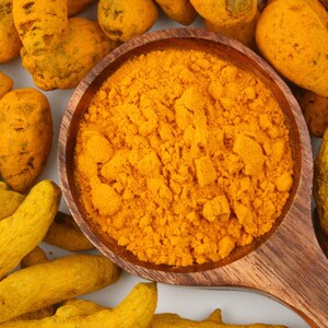 May include: A wooden spoon filled with bright yellow turmeric powder, surrounded by whole turmeric root pieces.