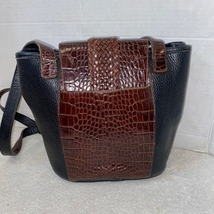 May include: A black and brown leather shoulder bag with a crocodile-embossed design. The bag has a flap closure with a braided strap.