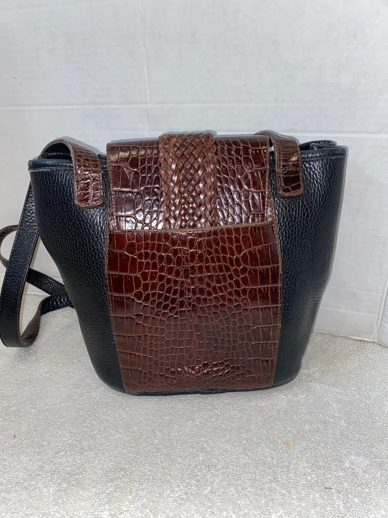 May include: A black and brown leather shoulder bag with a crocodile-embossed design. The bag has a flap closure with a braided strap.