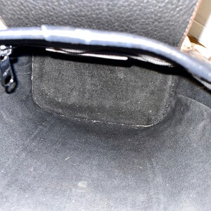 May include: The inside of a black leather bag with a zip closure. The bag is lined with a black fabric.