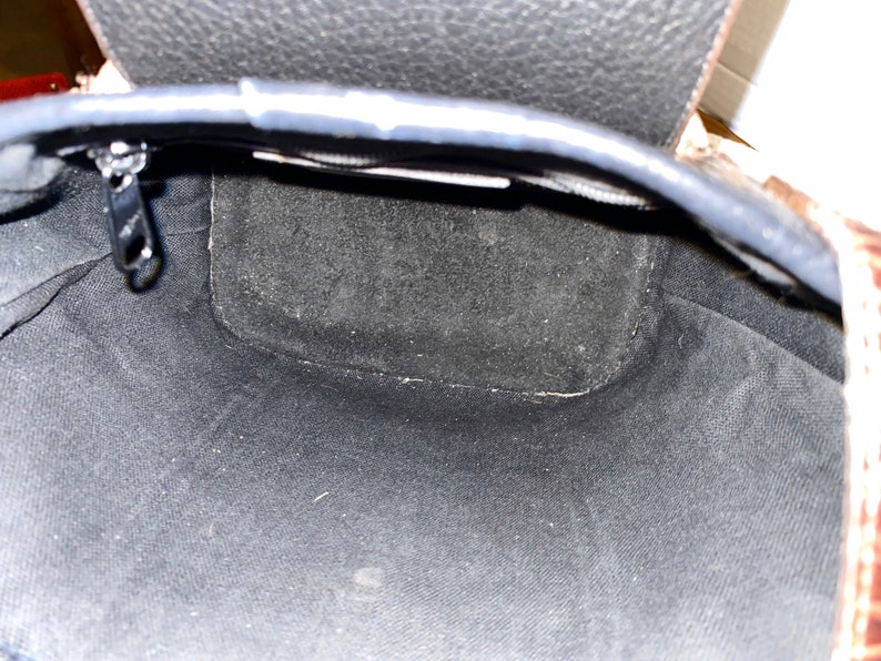 May include: The inside of a black leather bag with a zip closure. The bag is lined with a black fabric.