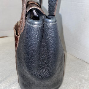 May include: A brown and black leather tote bag with a top handle and a zip closure.